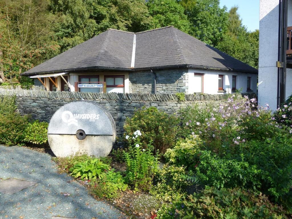 A stone building with a sloped roof, a sign indicating 'Quaysiders Club,' and a stone wall with a circular emblem.