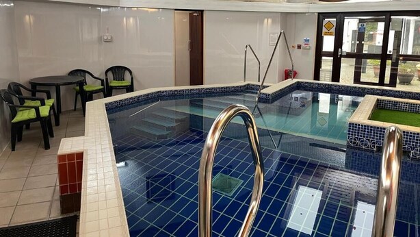 Una piscina interior con suelo de baldosas, una escalera de piscina y una puerta que da al exterior.