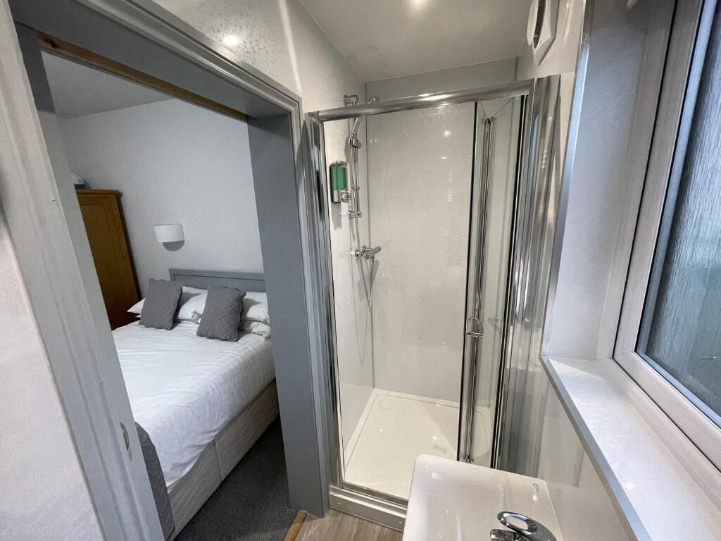 A compact room with a bed, a shower enclosure, and a sink.