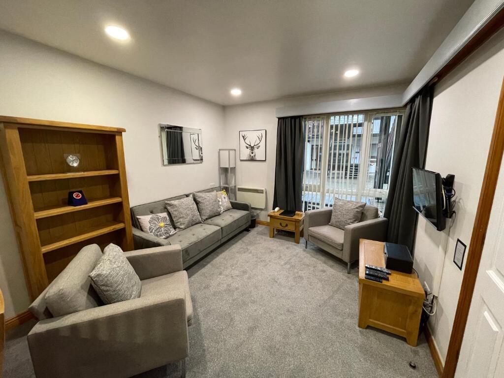 A modern living room with a sofa set, a wooden bookshelf, a television, and a window with curtains.