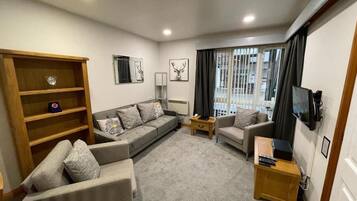 A modern living room with a sofa set, a wooden bookshelf, a television, and a window with curtains.