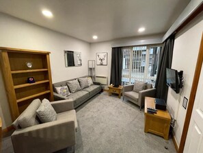 A modern living room with a sofa set, a wooden bookshelf, a television, and a window with curtains.