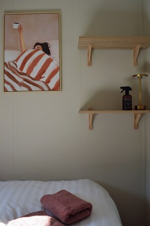 Ein Schlafzimmer mit einem Bett, einem Bild, einer Ablage mit einer Flasche und einer Lampe.