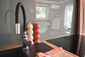 Eine Küchenzeile mit einem modernen Wasserhahn, einem Glastisch und Blick auf einen Essbereich durch ein Fenster.