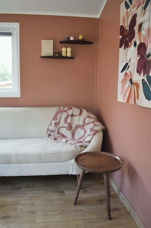 Ein Zimmer mit einer Couch, einem kleinen runden Holztisch, einem Fenster und einer Wand mit einem Blumenbild.