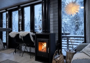 A cozy room with a wood-burning stove, large windows, and a view of a snowy landscape.
