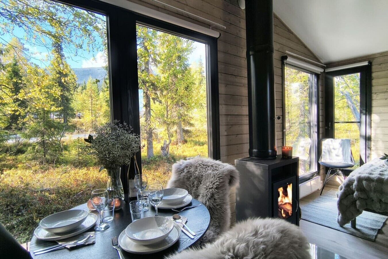 Un comedor con una mesa preparada para dos, una chimenea y vistas a un bosque.