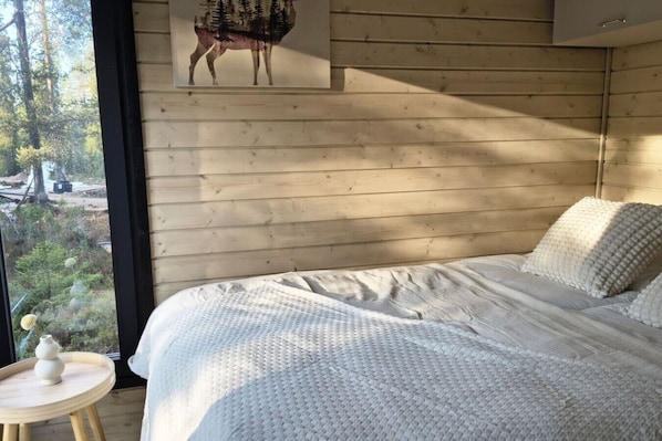 A bedroom with a large bed, wooden walls, a window with a view of trees, and a painting of a deer.
