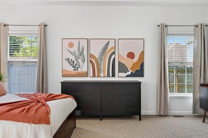 Un dormitorio con una cama, un aparador oscuro y tres obras de arte colgadas en la pared.