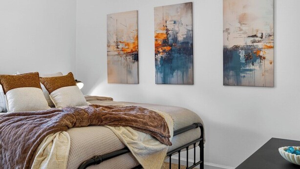 A bedroom with a bed, pillows, a blanket, and three abstract paintings on the wall. - Roadmap Lodging: Sumpter Stay, 3BR Monthly, Garage, Fenced Yard, Pet OK (Columbus)