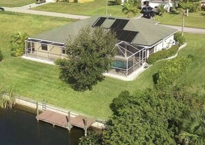 A house with a large deck and a swimming pool, surrounded by a well-maintained lawn and a body of water. - Villa Cimarron - Waterfront Pool Home, Kayaks & Bikes (Cape Coral)