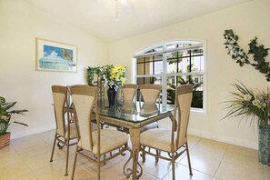 Uma sala de jantar com uma mesa de vidro rodeada por cadeiras de vime, um quadro na parede e uma janela com vista.
