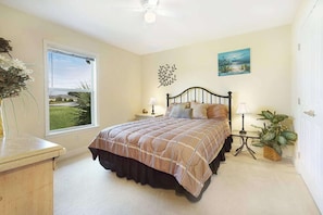 A bedroom with a bed, bedside tables, a window, a painting, and a plant. - Villa Cimarron - Waterfront Pool Home, Kayaks & Bikes (Cape Coral)