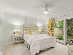 Ein Schlafzimmer mit einem Bett, Nachttischen, Lampen, einem Deckenventilator und Blick auf einen Garten durch eine Schiebetür.