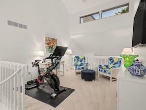 A room with a stationary bike, a white chair, a colorful painting, and a green vase. - Beautiful Breakers East Condo with Lake Michigan Views (Harbor Springs)