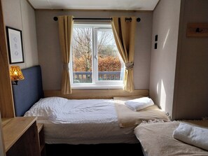 Ein Schlafzimmer mit einem Bett, einem Nachttisch, einer Lampe und einem Fenster mit Vorhängen.