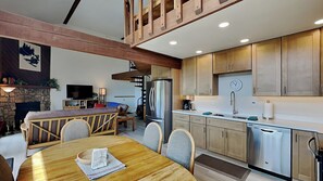 A modern kitchen with wooden cabinets, a stainless steel refrigerator, and a dining area with a wooden table and chairs. - NEW! Cozy escape with breathtaking treetop views (Silverthorne)