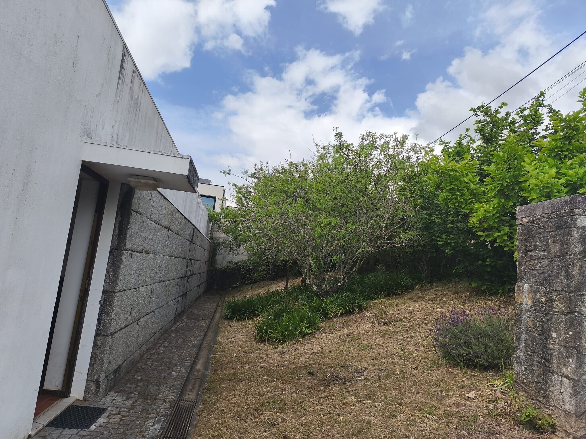 Un sendero estrecho que lleva a un edificio con fachada blanca y una pared de piedra a un lado.
