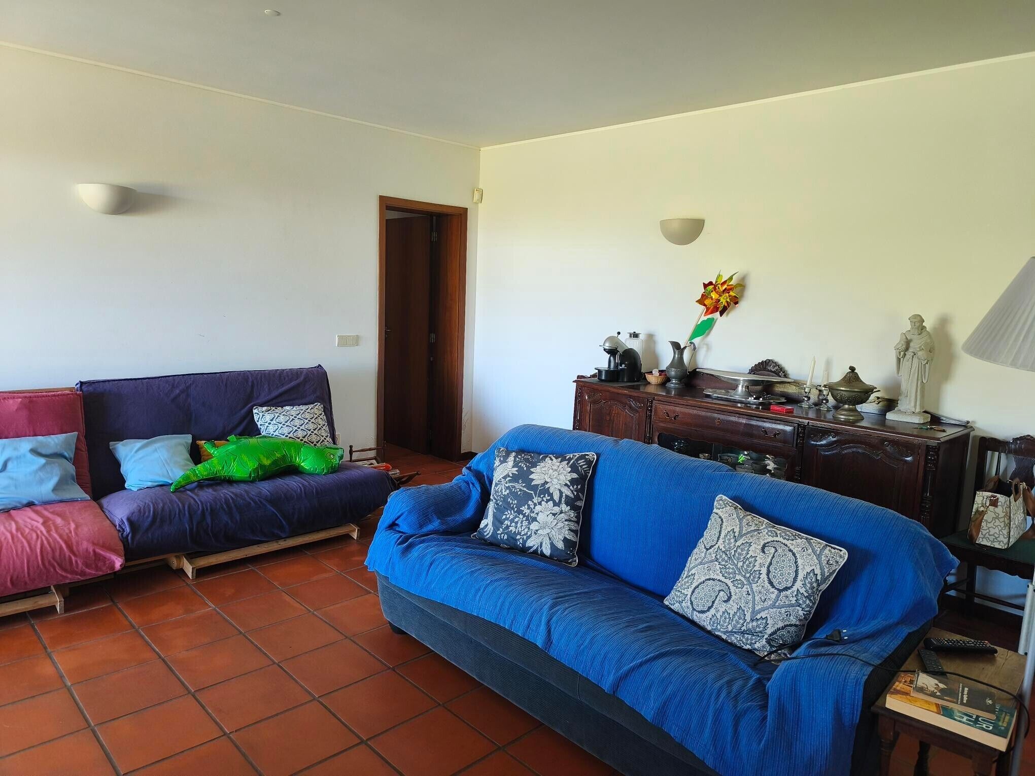 Una sala de estar con un sofá, un mueble de madera y una mesita con libros y un control remoto.