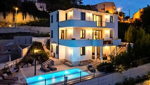 Une maison moderne à plusieurs étages, dotée d’une piscine, d’un espace salon extérieur et d’un escalier menant aux niveaux supérieurs.