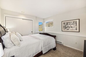 A bedroom with a bed, a nightstand, a window with a view, and a framed picture on the wall. - Panoramic rooftop deck, captivating views, and tranquil luxury (Dillon)