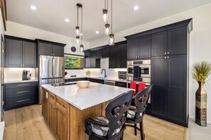 A modern kitchen with dark cabinetry, stainless steel appliances, and a central island with seating. - Panoramic rooftop deck, captivating views, and tranquil luxury (Dillon)