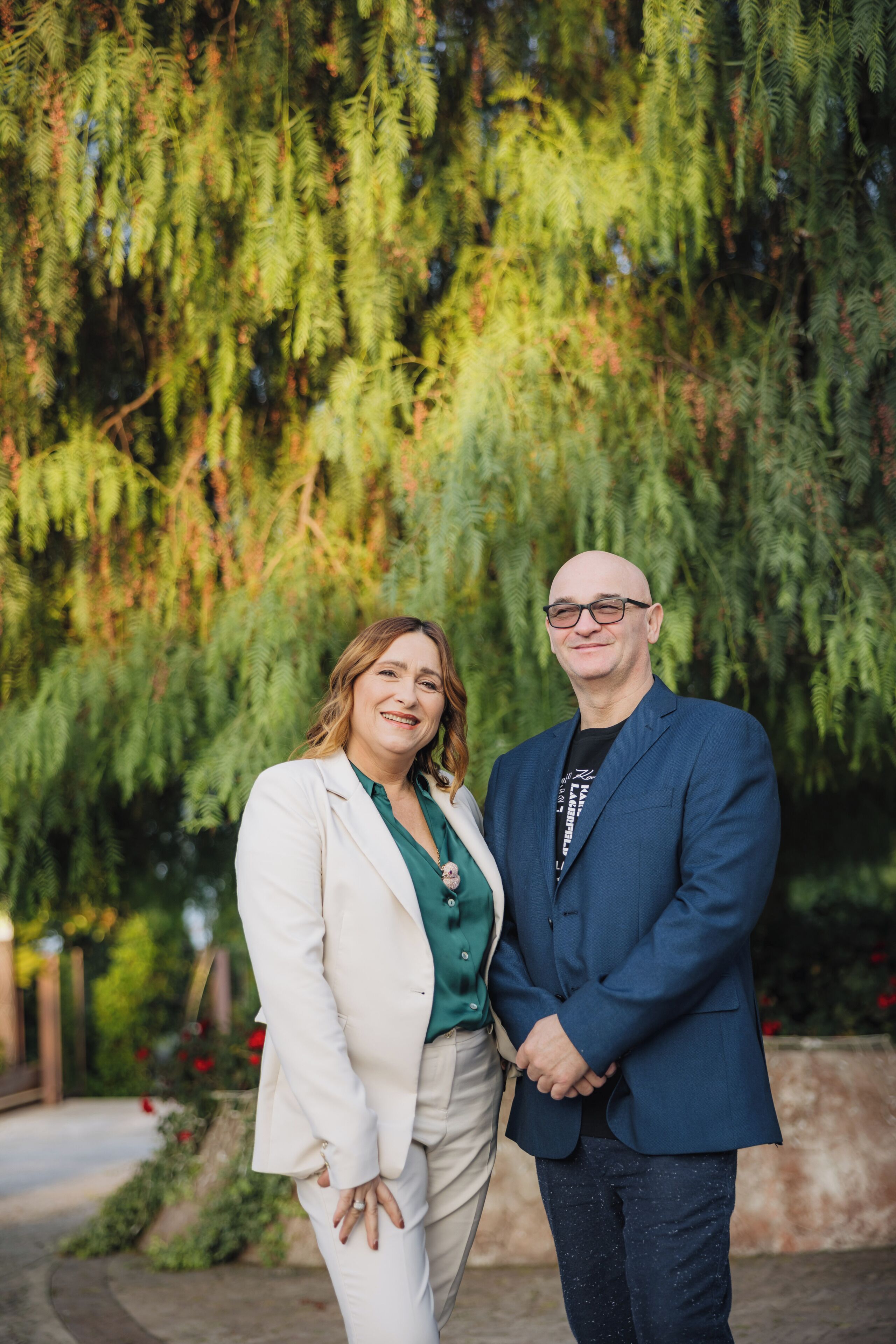 Two people standing in front of a tree with a blurred background.