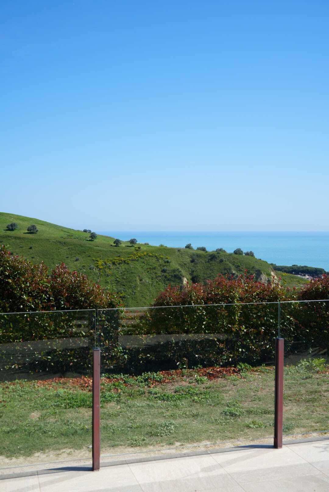Un paysage côtier avec un ciel dégagé, une colline herbeuse et une étendue d’eau à l’horizon.