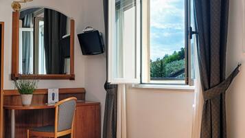 Una camera d'albergo con un letto, una scrivania con un computer, una televisione e una finestra con tende.