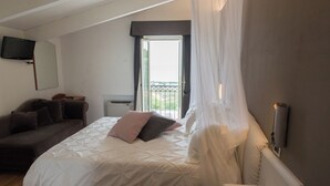 Un dormitorio con cama, sofá, televisión montada en la pared y una ventana con cortinas.