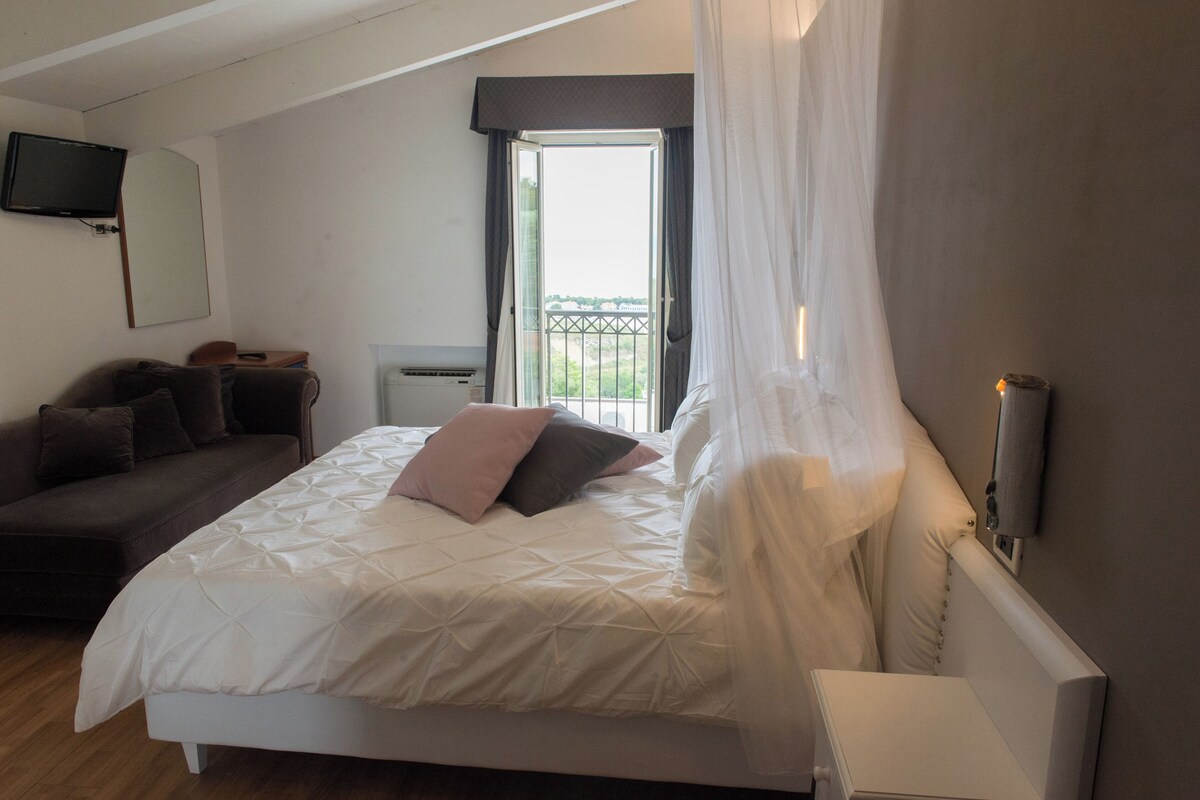 Un dormitorio con cama, sofá, televisión montada en la pared y una ventana con cortinas.