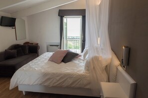 A bedroom with a bed, a sofa, a television mounted on the wall, and a window with curtains. - LA GRIGLIA DI CASA NOSTRA SRL (Silvi)