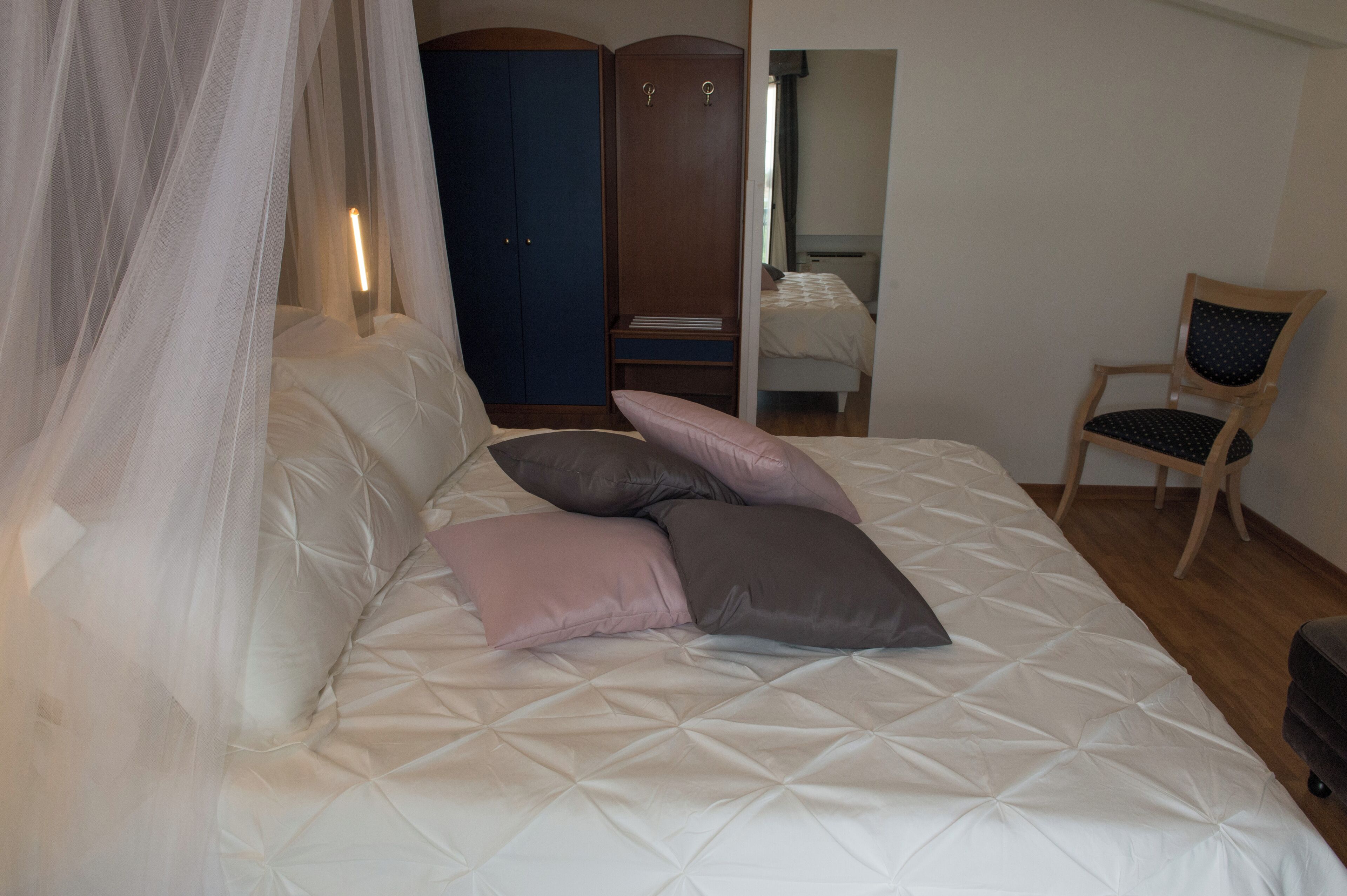Un lit à baldaquin, des oreillers, une armoire, une chaise et un miroir.