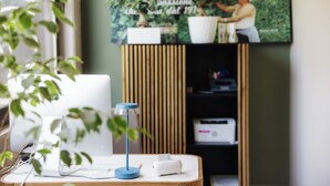 Un espacio de trabajo con una computadora portátil, una lámpara de escritorio e impresora sobre una mesa de madera.