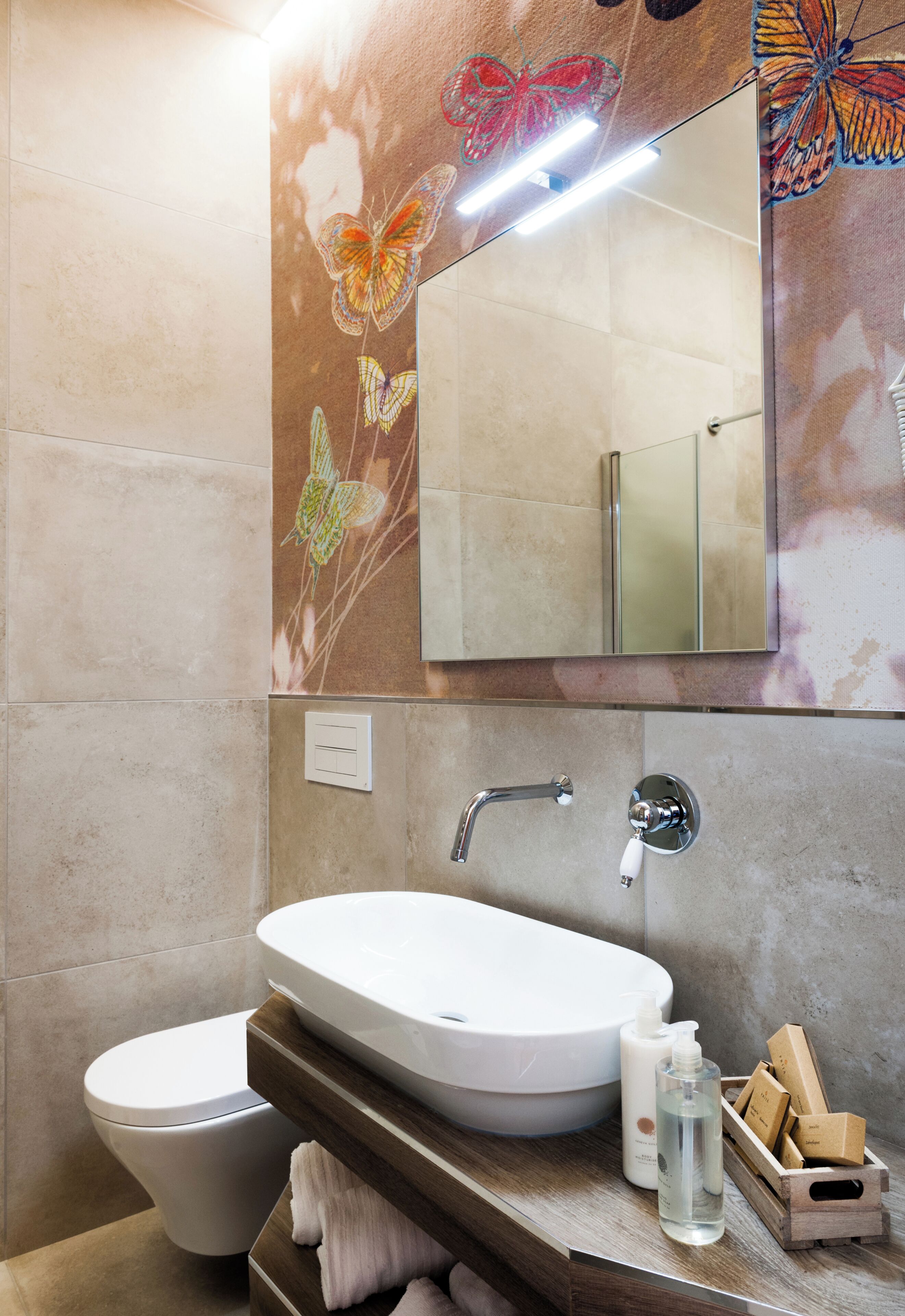 A bathroom with a white sink, a toilet, a mirror, and a wall with butterfly artwork.