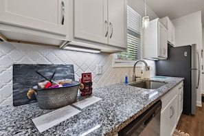 A kitchen with white cabinets, a granite countertop, a stainless steel sink, and a black refrigerator. - Yellowhammer | 1.8 Miles to Bryant-Denny Stadium (Tuscaloosa)