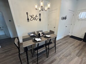 A dining area with a wooden table set for four, a chandelier, and a wall with 'Eat!' and 'Coffee' signs. - Yellowhammer | 1.8 Miles to Bryant-Denny Stadium (Tuscaloosa)