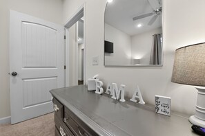 A room with a closed door, a vanity with drawers, a mirror, a ceiling fan, a flat-screen TV, and a motivational sign. - Yellowhammer | 1.8 Miles to Bryant-Denny Stadium (Tuscaloosa)