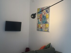 A room with a flat-screen TV mounted on the wall, a colorful abstract painting, and a green sofa with cushions. - Cozy, self-contained apartment just a few minutes from the historic center of Lecce (Lecce)
