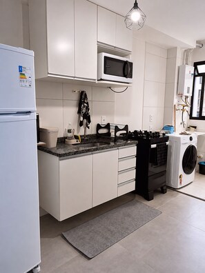 A modern kitchen with white cabinets, a built-in microwave, a gas stove, and a washing machine. - BEACH WALKABLE Charming 2-bedroom apartment with AC in enchanting Rio (Rio de Janeiro)
