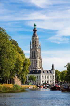 A historic church with a tall spire, a river in the foreground, and a building with a green roof across the river.
