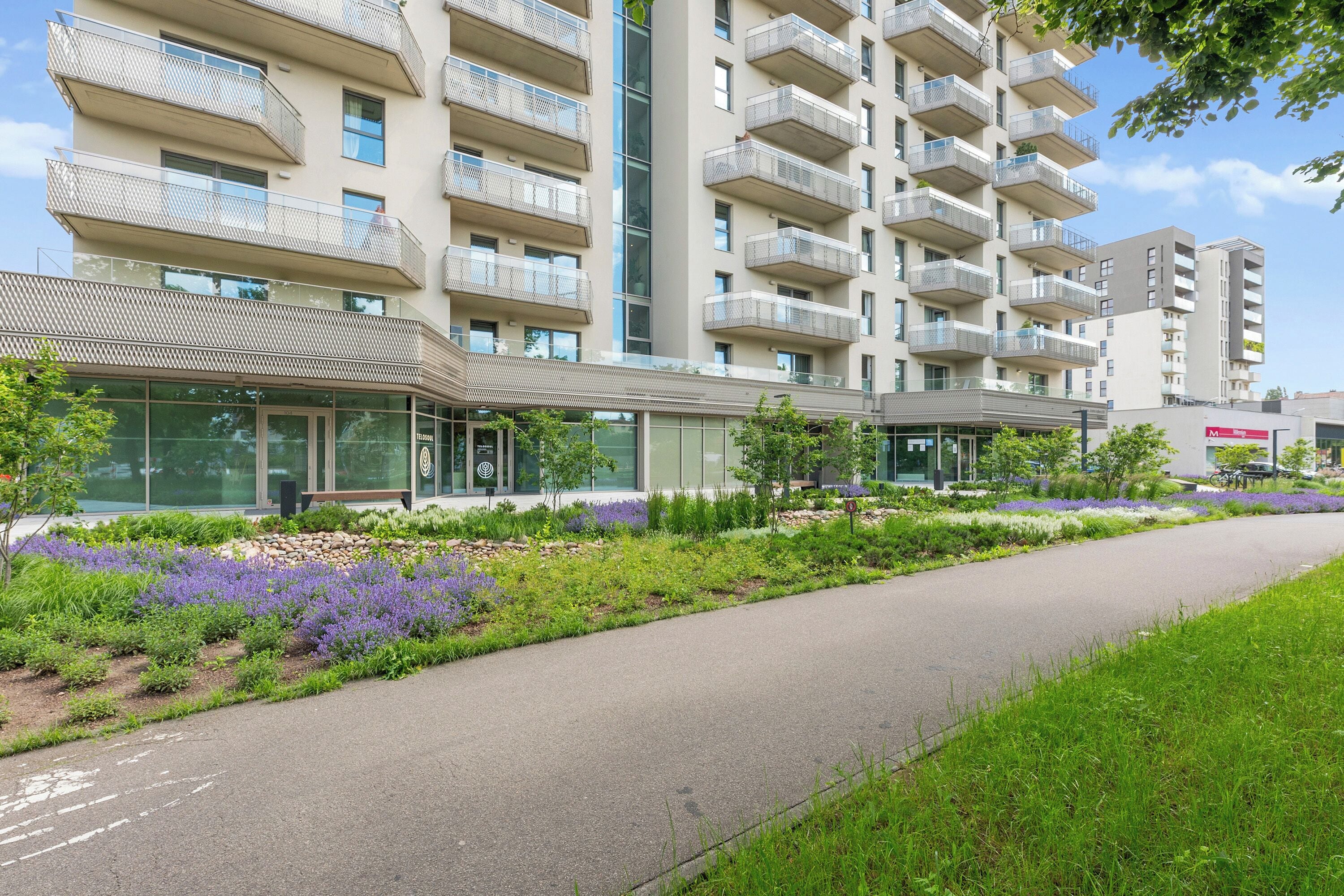 A modern building with multiple balconies and a landscaped garden area.