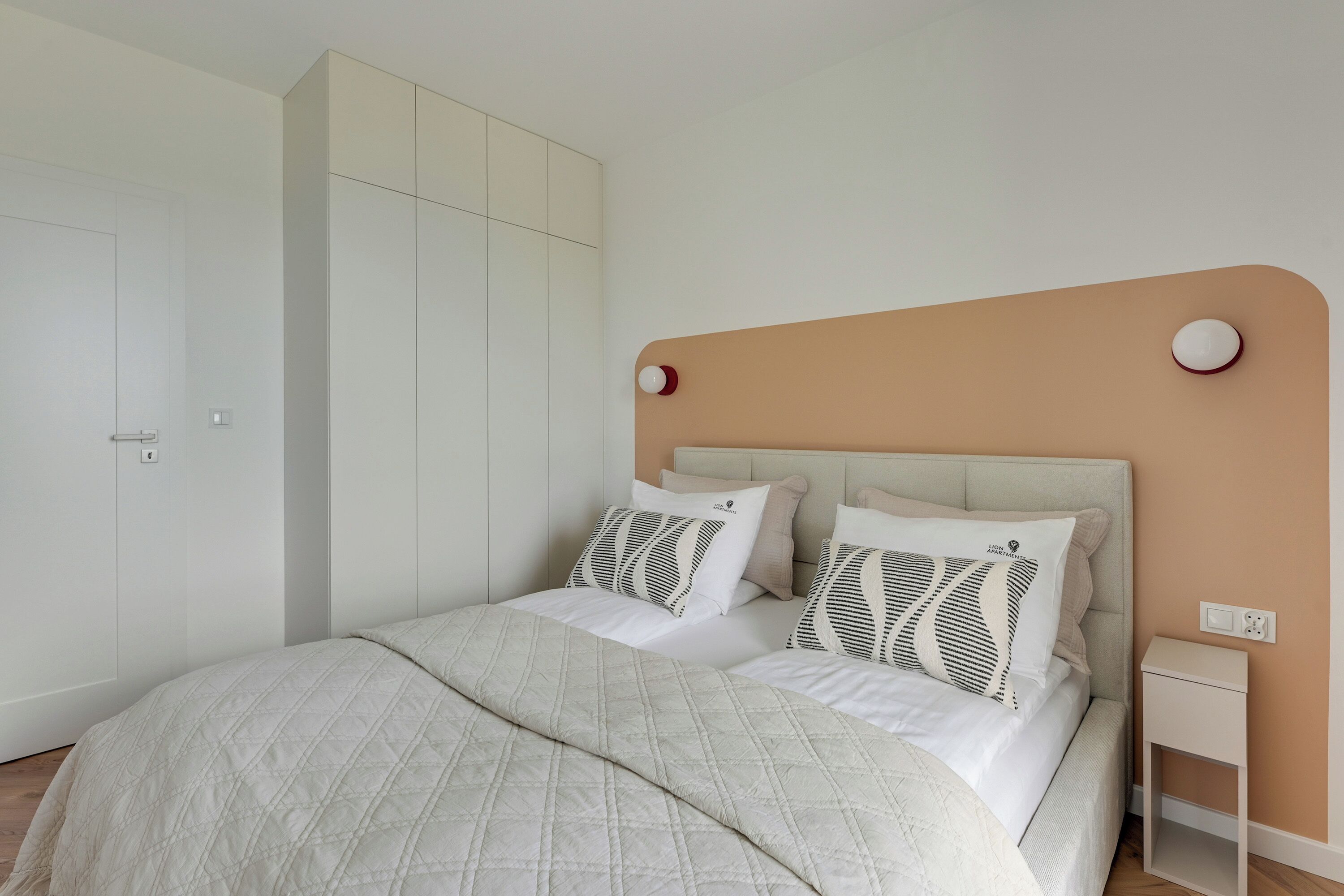 A bedroom with a bed, two bedside tables, a wardrobe, and a wall-mounted light fixture.