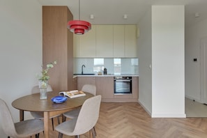 A modern kitchen with wooden cabinets, a built-in oven, and a dining area with a round table and chairs.