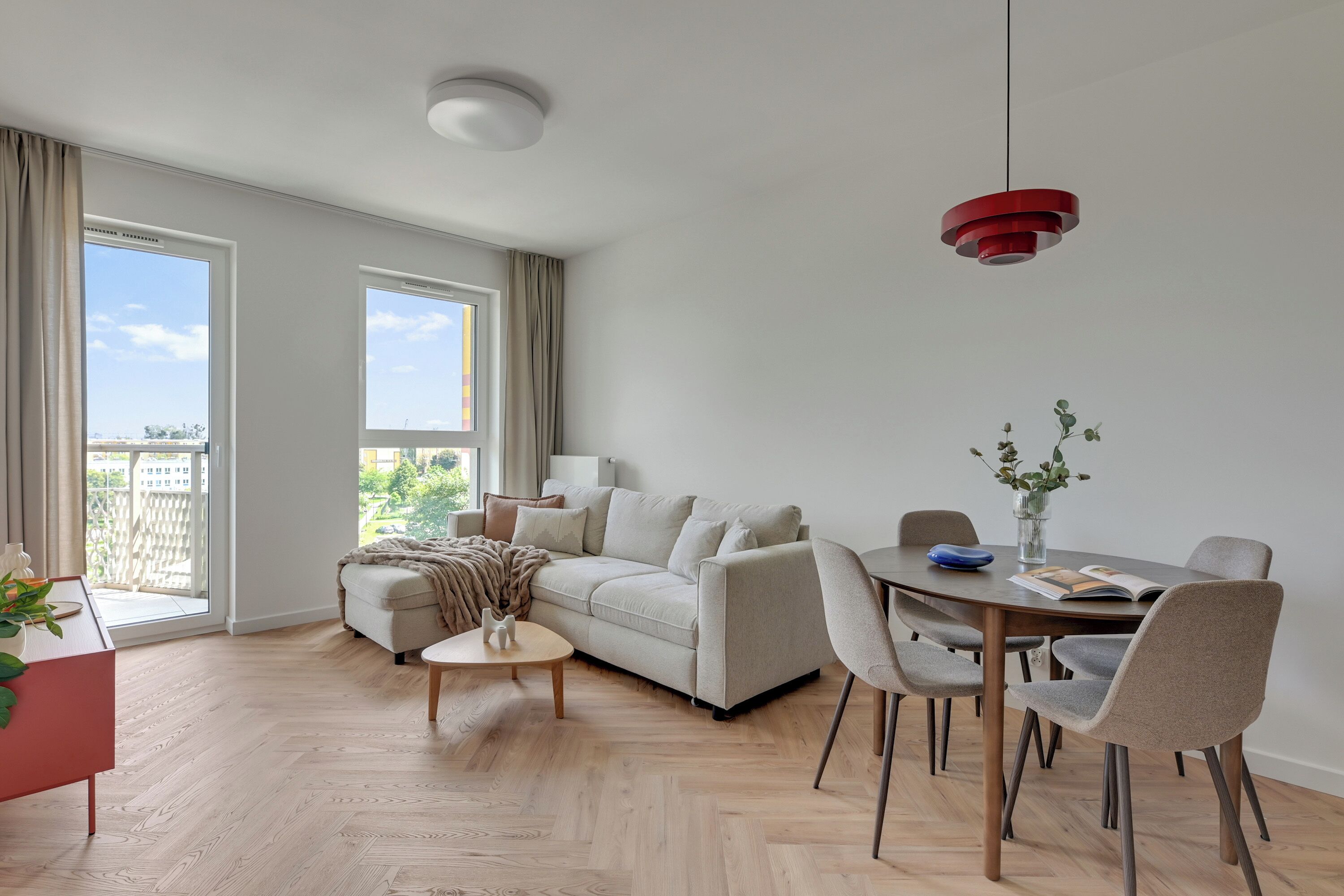 Una sala de estar moderna con un sofá, una mesa de centro, una mesa de comedor con sillas y una lámpara colgante roja.
