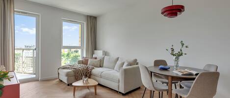 Una sala de estar moderna con un sofá, una mesa de centro, una mesa de comedor con sillas y una lámpara colgante roja.