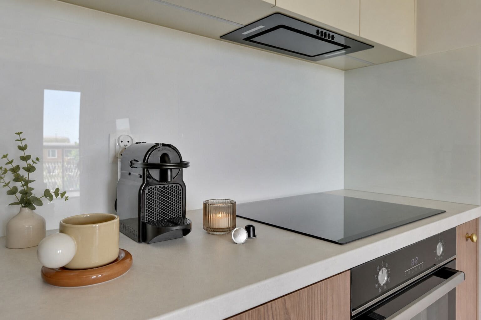Una cocina moderna con cafetera, una vela y un florero con plantas sobre la encimera.
