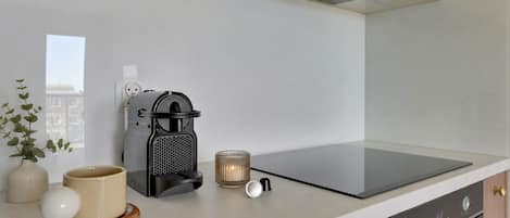 Una cocina moderna con cafetera, una vela y un florero con plantas sobre la encimera.
