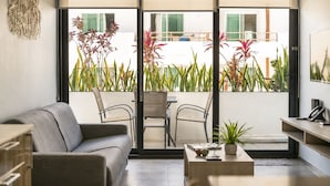 Een moderne woonkamer met een bank, stoelen, een salontafel en uitzicht op een balkon met planten.