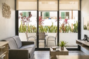 A modern living room with a sofa, chairs, a coffee table, and a view of a balcony with plants. - One Bedroom Apartment (Playa Del Carmen)